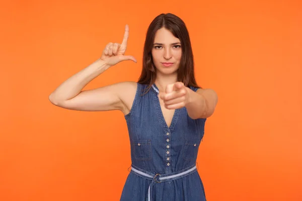 Bossy kvinna i denim klänning visar L-tecken och pekar på kameran — Stockfoto