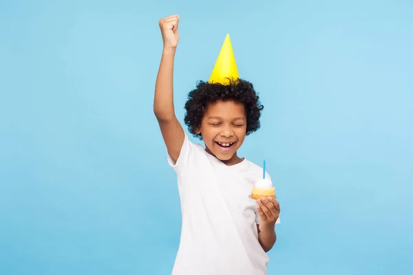 Entusiasmado menino feliz com festa cone segurando cupcake e k — Fotografia de Stock