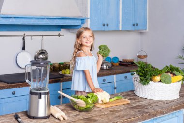 Sevimli küçük kız elinde sebzelerle kameraya bakıyor.