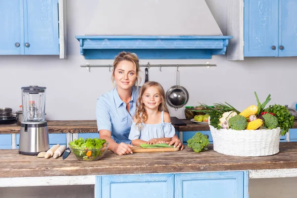 Young woman and lovely girl sitting in modern kitchen, looking a — Stock Photo, Image