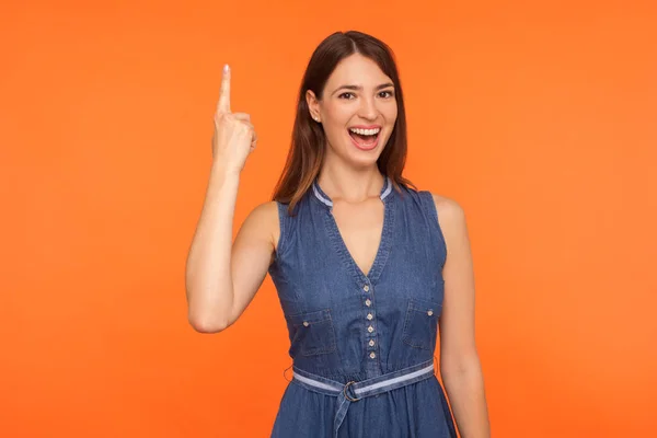 Smart Brünette Frau im Jeanskleid zeigt mit erhobenem Zeigefinger nach oben — Stockfoto