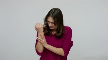 Frustrated woman rubbing injured hand with painful facial expression, massaging sore wrist,