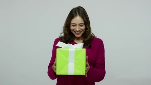 Aufgeregte brünette Frau im Pullover lächelt und schüttelt Box und hört zu erraten, was drin ist — Stockvideo