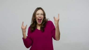 Yeah, that's crazy! Excited overjoyed brunette woman roaring aggressively and showing rock and roll hand gesture