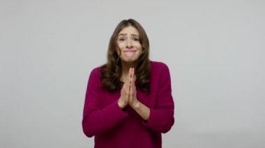 Please, I need! Cute beseeching brunette woman in pullover holding hands in prayer and pleading to camera