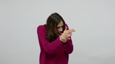 Funny woman in pullover aiming with finger pistol, looking around for target, making shot with handgun gesture