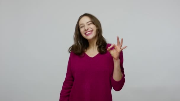 Я в порядке! Радостная симпатичная брюнетка в пуловере улыбается довольно и показывает нормальный жест — стоковое видео