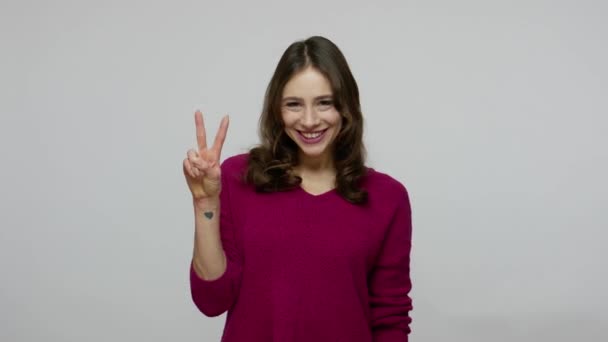 Winning and success concept. Happy nice-looking brunette woman in pullover showing victory gesture and smiling — ストック動画