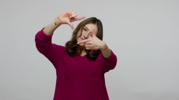 Vrolijke brunette vrouw in pullover op zoek door fotolijstje gemaakt van vingers — Stockvideo