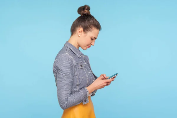 Seitenansicht einer leicht buckligen Frau mit Haarknödel mittels Handy — Stockfoto