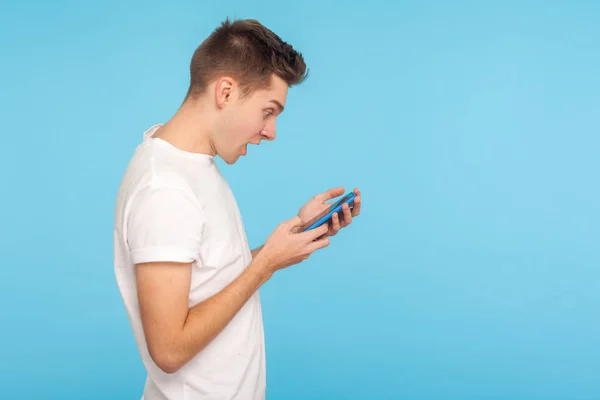 Side view of amazed astonished man in t-shirt using cellphone wi — Stok fotoğraf