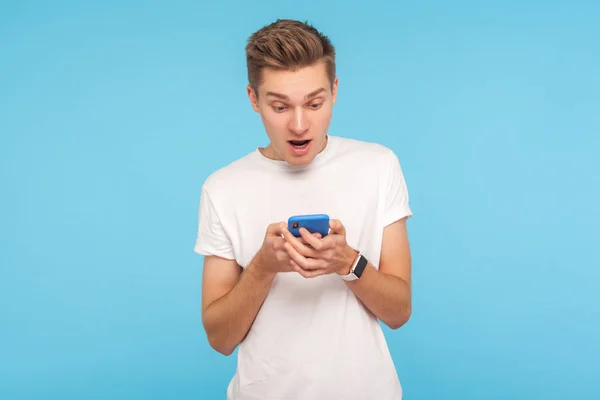 Portrait of amazed astonished man in white t-shirt using cellpho — Stok fotoğraf