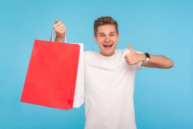 Happy enthusiastic shopper in T-shirt holding packages and showi