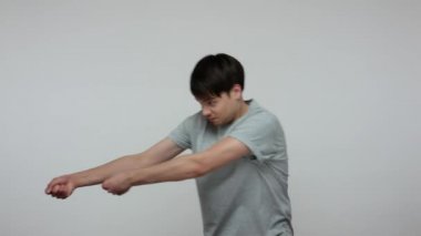 Young ambitious guy in T-shirt holding invisible rope and pulling his burden with great effort, metaphor for difficult path to success, strivings and motivation. Indoor studio shot gray background.