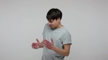 Cheerful happy young brunette man in T-shirt dancing like robot, performing robotic moves to rhythm of music, enjoying favorite song and having fun. indoor studio shot isolated on gray background