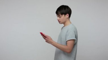 Web browsing on mobile internet. Serious focused guy in t-shirt using smartphone, scrolling pictures on social networks, commenting, reading blog. indoor studio shot isolated on gray background
