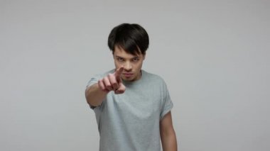 Hey you! Rigid strict brunette man in T-shirt pointing to camera and looking angrily with suspicion, blaming for failure, choosing guilty person. indoor studio shot isolated on gray background