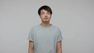 Happy young ambitious student guy in casual T-shirt dreaming of successful future career and smiling, having optimistic fantasies, positive memories. indoor studio shot isolated on gray background