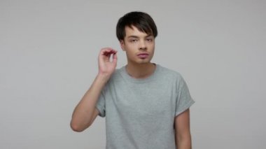 Young guy with hearing problems holding hand near his ear and listening around carefully, being focused attentive to sounds, trying to hear conversation. indoor studio shot isolated on gray background