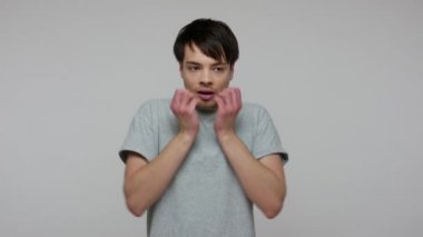 Nervous depressed man with worried expression biting nails, thinking anxiously about problems, looking terrified scared, panicking over troubles. indoor studio shot isolated on gray background