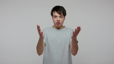Frustrated angry guy in T-shirt shouting, scolding to camera, gesturing what do you want from me, having troubles in relations, misunderstanding and breakup. studio shot isolated on gray background