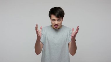 Kızdırma beni! Tişörtlü sinirli esmer adam nefretle konuşuyor, öfkesini ve sinirini zar zor dizginliyor, kızgın görünen yumrukları sıkıyor. Gri arka planda kapalı stüdyo çekimi