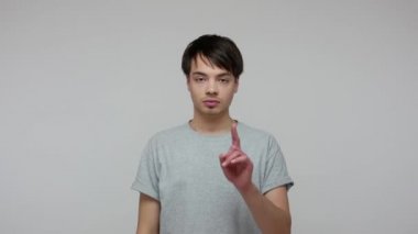 Annoyed dissatisfied brunette guy in T-shirt showing loser gesture, making L sign with fingers, pointing to camera meaning you lost, blaming for failure. indoor studio shot isolated on gray background