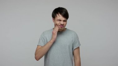 Oral health, dental problems. Young brunette guy with sensitive teeth feeling sharp pain in mouth, suffering from tooth decay, inflammation of gum. indoor studio shot isolated on gray background
