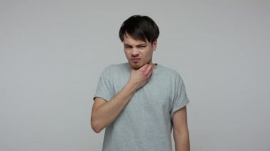 Neck pain. Young brunette man having sore throat, respiratory infection with larynx inflammation, hard to swallow, suffering from thyroid disorder. indoor studio shot isolated on gray background