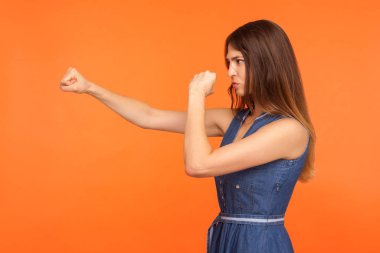 Kavgacı ruhlu kararlı esmer kız yumruklarla, boksla yumruk atan, kendine güvenen ve güçlü görünen, kendini savunan. Stüdyo çekimi turuncu arkaplanda izole edildi