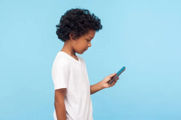 미취학 아이의 티셔츠를 스마트폰으로 모바일 미디어를 사용하는 스튜디오 가파란 배경에 — 스톡 사진