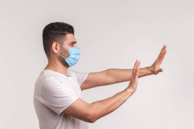 Hijyenik koruyucu maske takmış, koronavirüs enfeksiyonundan korkan, 2019-Ncov gibi solunum hastalıklarından korkan bir adamın yan görüntüsü. Beyaz arka planda izole edilmiş kapalı stüdyo çekimi