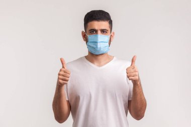 Bulaşıcı hastalıklara karşı etkili bir koruma. Enfeksiyonu önlemek için baş parmak gösteren ve hijyenik maske takan adam. Grip, koronavirüs gibi solunum hastalıkları. Kapalı stüdyo çekimi, izole.