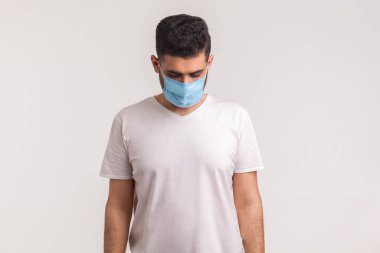 Hijyen maskeli hasta bir adam üzgün, koronavirüs enfeksiyonundan korkmuş ve çaresiz bir şekilde aşağıya bakıyor. Grip gibi hava yoluyla bulaşan solunum hastalıkları, 2019-ncov, ebola. Stüdyo çekimi beyaz arkaplanda izole edildi