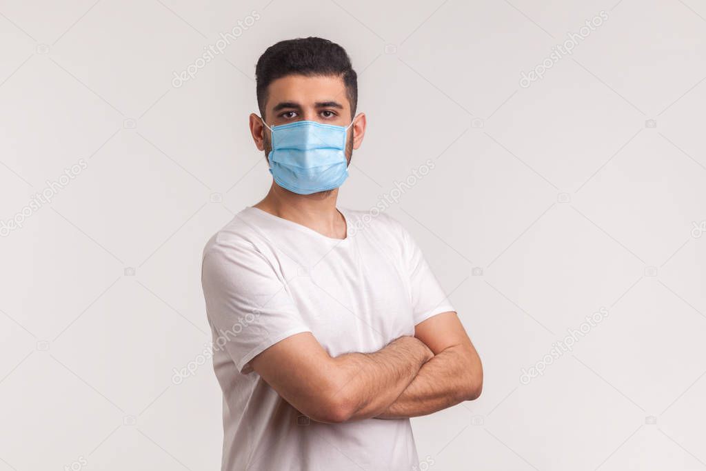 Effective protection against coronavirus. Man holding hands crossed and wearing hygienic mask to prevent infection, respiratory illness such as flu, 2019-nCoV. indoor studio shot, white background