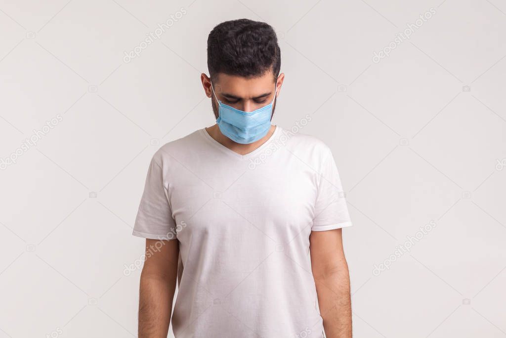 Sick man in hygienic mask looking down sadly, scared and desperate about coronavirus infection, airborne respiratory illness such as flu, 2019-nCoV, ebola. studio shot isolated on white background