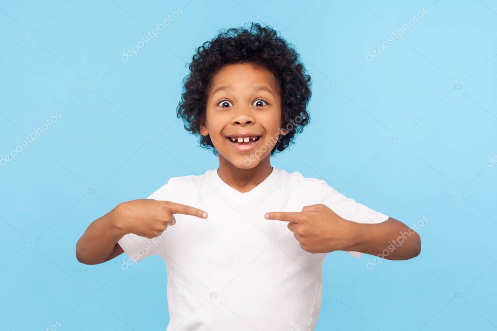 Wow, this is me! Portrait of amazed happy preschool boy in T-shirt looking at camera with shocked face and pointing himself, being proud and surprised. indoor studio shot isolated on blue background