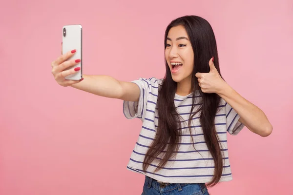 满意的友善的亚洲女孩的画像 一头乌黑的头发 竖起大拇指 通过视频通话和网上聊天 在粉红背景下隔离的室内拍摄 — 图库照片