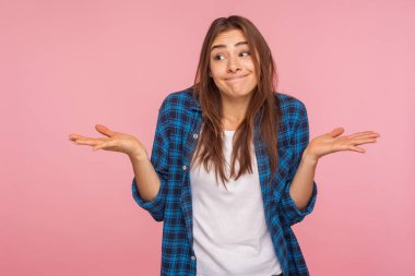 Cevap veremiyorum! Kareli tişörtlü, kafası karışmış, utangaç ifadesiyle omuzlarını silken, şüpheleri olan, emin olamayan komik bir kızın portresi. Pembe arka planda kapalı stüdyo çekimleri