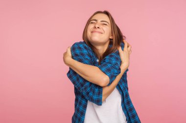 Kendimi seviyorum! Kareli gömlekli çekici bir kızın portresi kendine sıkıca sarılıyor ve zevkle gülümsüyor, görünüşünü takdir ediyor, kendine saygı kavramını takdir ediyor. Stüdyo çekimi pembe arkaplanda izole edildi