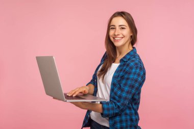 Serbest çalışan gülümseyen bir işçinin portresi, sıradan tişörtlü mutlu bir kız elinde dizüstü bilgisayar, eğitim ya da internet işi için bilgisayar kullanıyor, internette geziniyor. Pembe arka planda kapalı stüdyo çekimleri