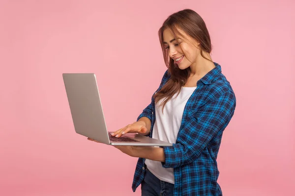 教育やオンラインの仕事のためのコンピュータを使用して ラップトップ上でフリーランスのタスクを行うカジュアル小切手シャツで笑顔の女性の肖像画 インターネットを閲覧 ピンクの背景に隔離された屋内スタジオで — ストック写真