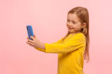 Çok güzel bir kızın portresi, çilli ve kızıl saçlı akıllı telefona gülümseyen, selfie çeken ya da anne babasıyla görüntülü konuşma yapan. Pembe arka planda kapalı stüdyo çekimleri
