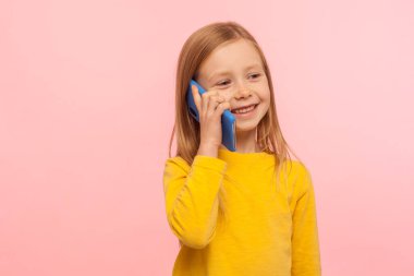 Yüzünde çilli, mutlu bir şekilde gülümseyen sevimli, cep telefonuyla ebeveynlerini arayan, cep telefonuyla gezen, gezen, çocuk cep telefonu kullanmak için rahat bir kız. Stüdyo çekimi pembe arkaplanda izole edildi