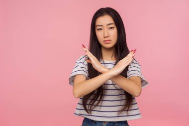 Olmaz, kes şunu! Esmer saçlı, çizgili tişörtlü ciddi bir kızın portresi. Çarpraz elli X işareti yapıyor. Duruyor, tehlike uyarısı yapıyor. Pembe arka planda kapalı stüdyo çekimleri