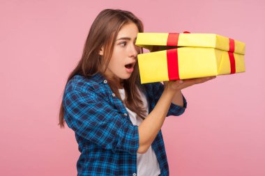 Portrait of curious amazed girl in checkered shirt looking inside present box with astonished shocked expression, pleasantly surprised by birthday gift. indoor studio shot isolated on pink background clipart