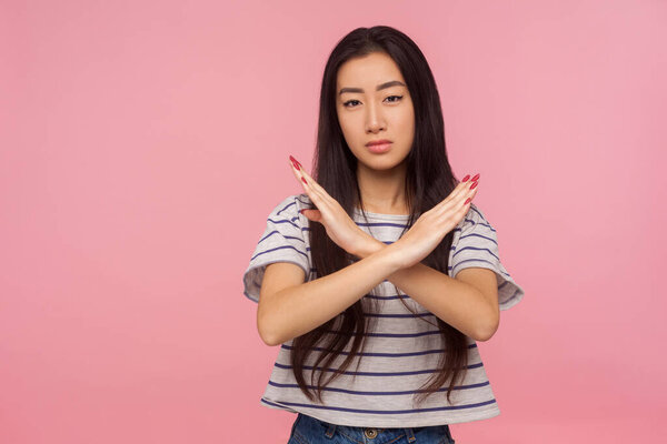 No way, stop doing! Portrait of serious girl with brunette hair in striped t-shirt making x sign with crossed hands, gesturing stop, warning of danger. indoor studio shot isolated on pink background