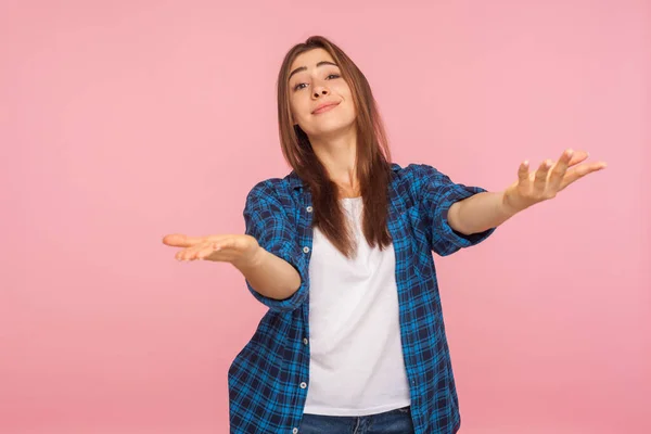 Portrait of generous kind-hearted girl in checkered shirt raising arms in gesture take everything for free, give me hug, looking hospitable and friendly. indoor studio shot isolated on pink background