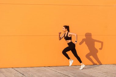 Dar spor giyimli, siyah pantolonlu ve üstsüz, motive olmuş, kendine güvenen bir sporcu. Koşmaya başlıyor, turuncu duvara doğru koşuyor, reklam alanına doğru koşuyor. Sağlık ve kilo kaybı, spor aktivitesi