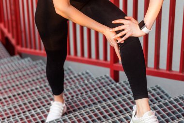 Spor kıyafetleri içinde kadın koşucunun merdivenleri çıkarken dizini tutması, bacağına dokunması, kas zorlanması, burkulmuş bağlarla yürümek, spor antrenmanında eklem yaralanması..